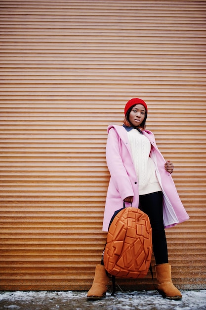 African american girl in red hat and pink coat with backpack against orange shutters