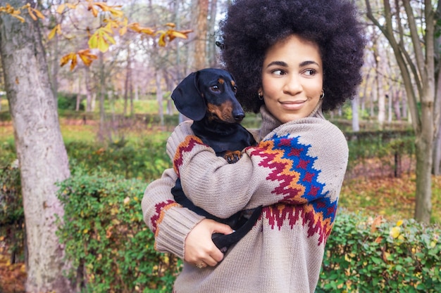 African American girl sitting and hugging her dog in the park in autumn