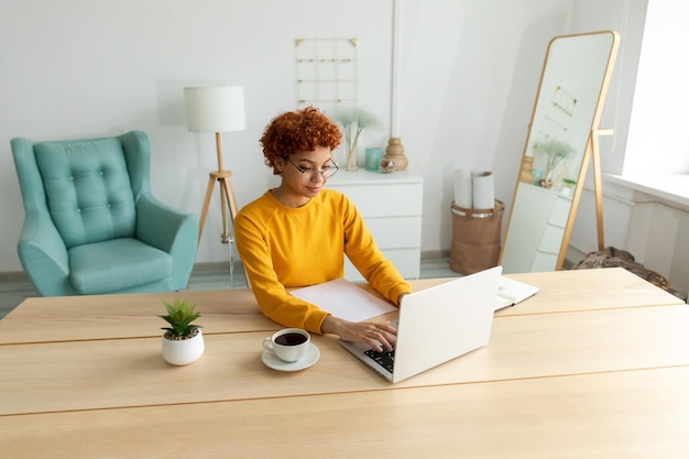 African american girl using laptop at home office looking at screen typing chatting reading writing