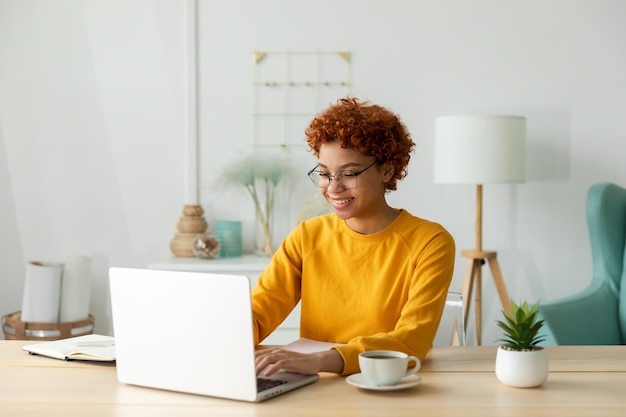 African american girl using laptop at home office looking at screen typing chatting reading writing