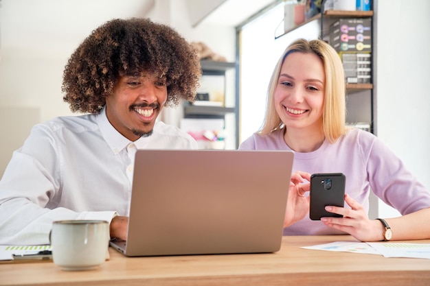 African American guy and Caucasian girl in a coworking sitting working on a laptop smiling