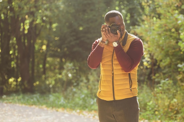 African american guy photographer taking picture with photo camera on city green park copy space leisure activity diversity and hobby concept