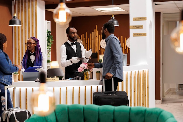 African American hotel receptionist talking with guest, confirming reservation details. Front desk staff checking in tourists arriving at resort during holiday season, customer service in hospitality