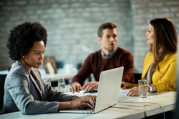 African American insurance agent using computer while being on in the office with her clients The couple is in the background