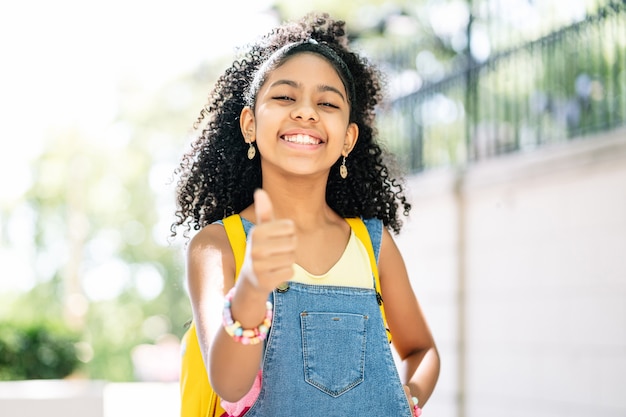 African American little girl smiling and with thumb up while wearing a backpack on the street