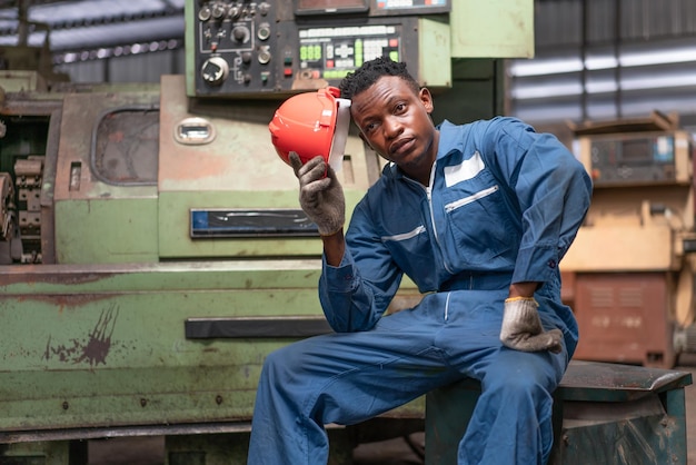 African American male engineer worker sitting on old machine feeling tired from work hard at factory