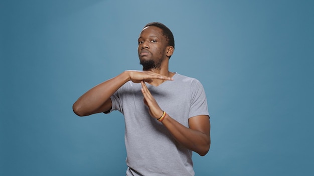 African american man doing timeout gesture with t shape hands, expressing half time and break, declining work. Serious person advertising pause symbol with palms, stop and refuse control.