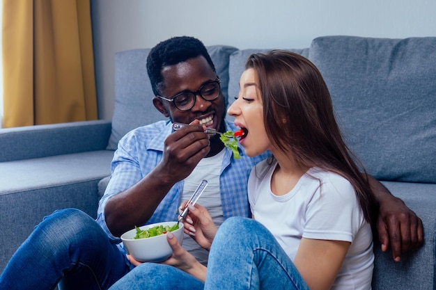 African american man eating salad with woman in living room