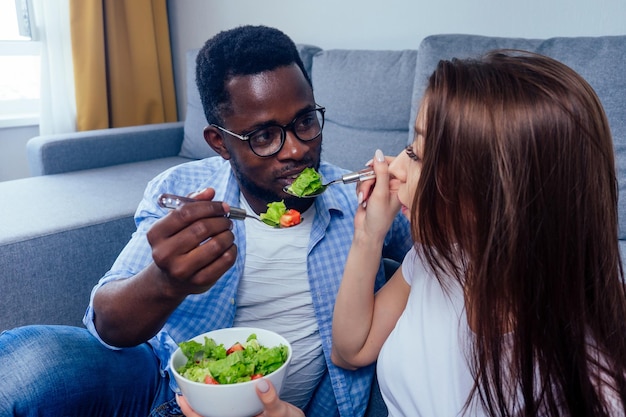 African american man eating salad with woman in living room