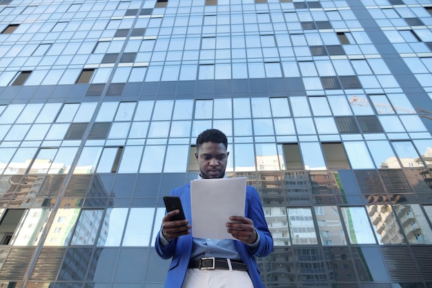 African american man examines papers checking with phone