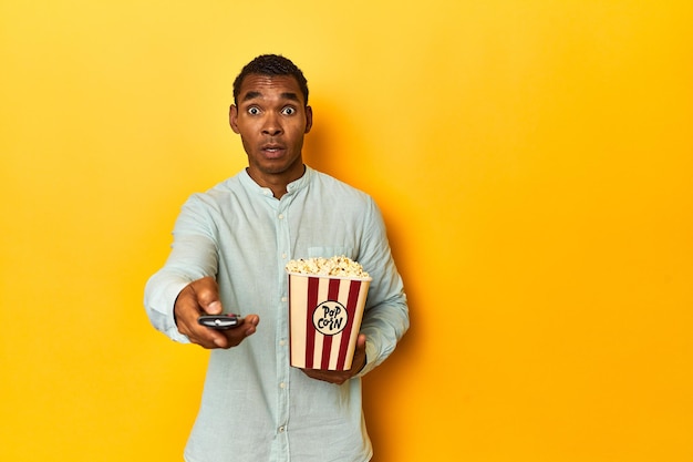 African American man holding popcorn in yellow studio backdrop