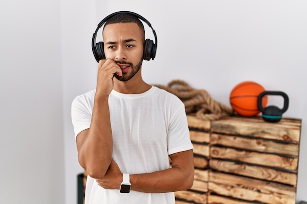 Photo african american man listening to music using headphones at the gym looking stressed and nervous with hands on mouth biting nails. anxiety problem.