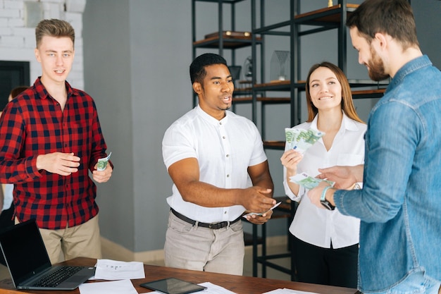 African American man manager giving salary in cash to happy employees Concept of money rain