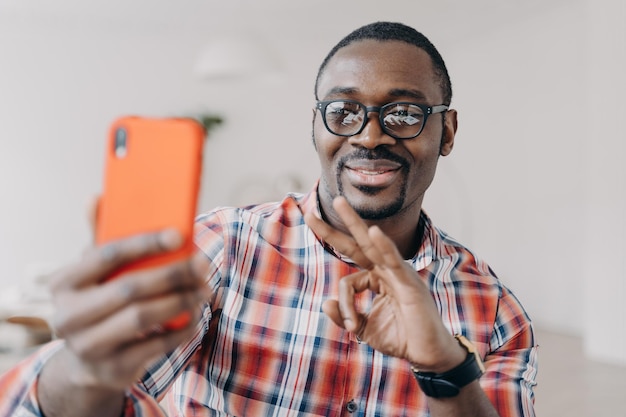 African american man shows ok approving gesture by hand holding phone communicates by video call