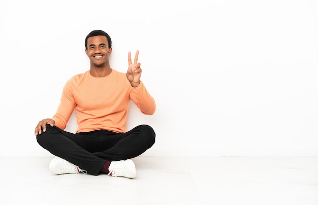 African American man sitting on the floor over isolated copyspace wall smiling and showing victory sign