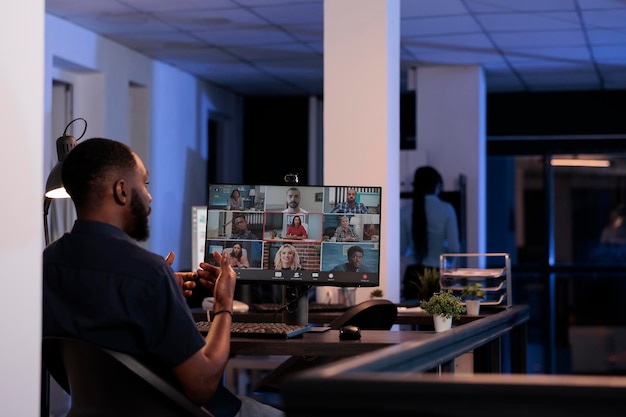 African american man talking to coworkers on remote videoconference call, using online teleconference meeting to discuss about business. Chatting on internet videocall with webcam at night.