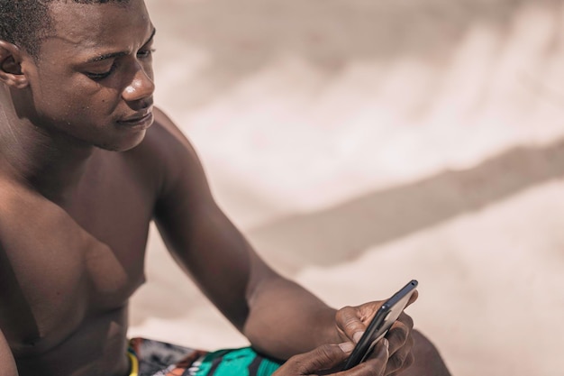 African american man using smartphone on the beach