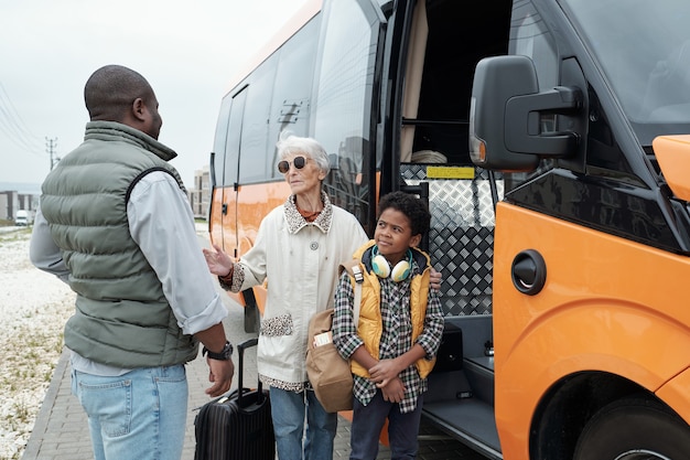 African american man in vest putting grandma and son on bus and listening to grandmothers promise