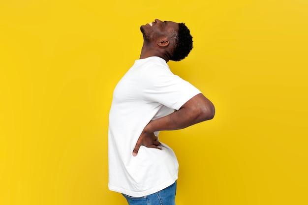 African american man in white tshirt holding on to his back and bending over yellow background