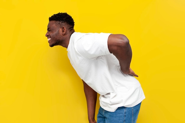 african american man in white tshirt holding on to his back and bending over yellow background