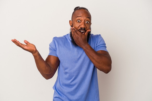 African american man with beard isolated on pink background holds copy space on a palm, keep hand over cheek. Amazed and delighted.