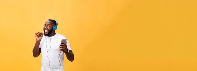 African american man with headphones listen and dance with music isolated on yellow background