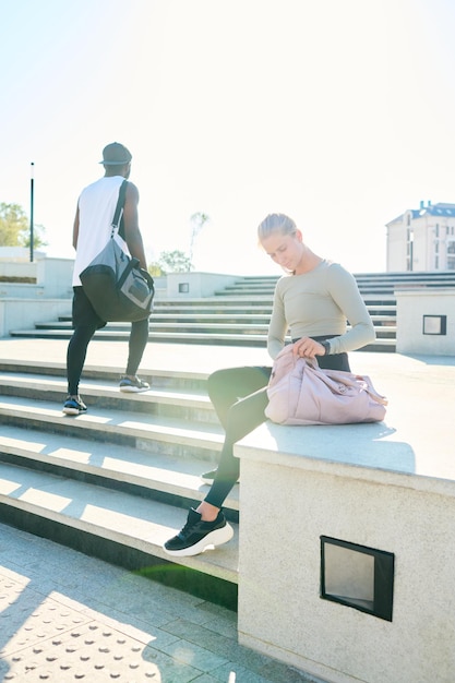 African american man with sport bag passing by girl sitting on concrete edge