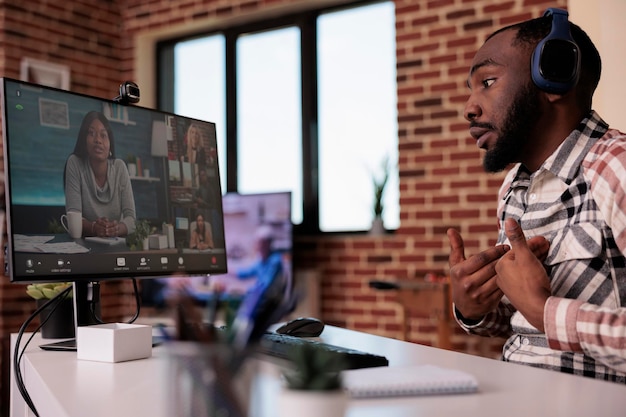 African american man with wireless headphones in online interview with startup owner and human resources team. Team brainstorming business ideas in video call conference working remote from home.