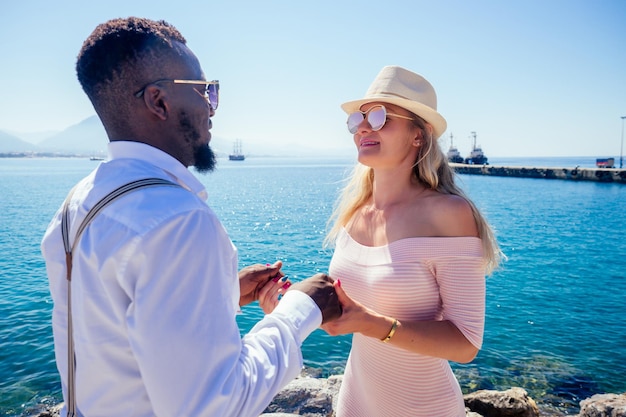 African american man and a woman look lovingly at each in summer tropical cafe and drinking fresh fruit orange cocktail.