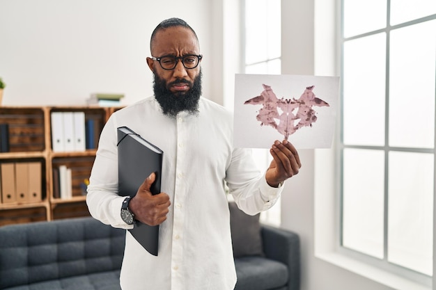 African american man working with rorschach test at psychology clinic skeptic and nervous frowning upset because of problem negative person