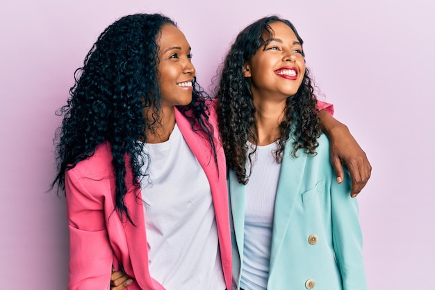 African american mother and daughter wearing business style looking away to side with smile on face, natural expression. laughing confident.