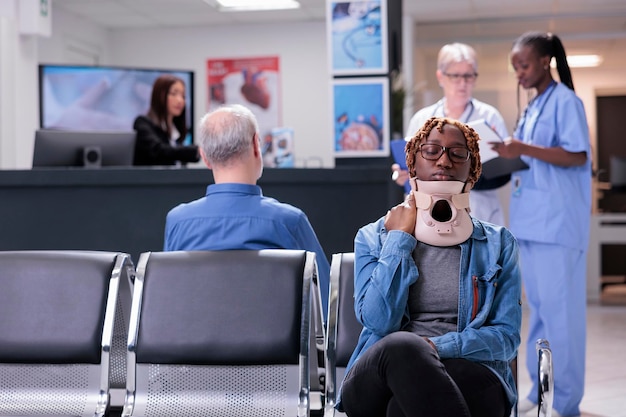 African american patient with neck collar sitting in hospital waiting room to attend checkup examination. Young adult with injury having consultation appointment with specialist at health center.