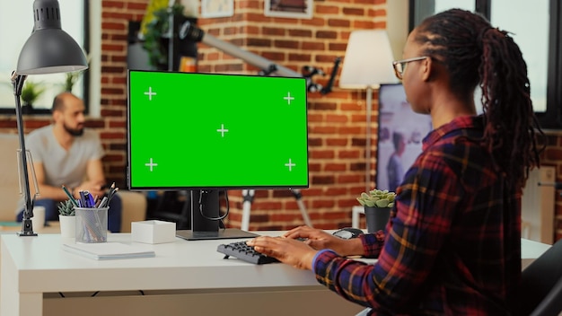 African american person using monitor to check with greenscreen template on isolated display, looking at chroma key background with mockup. Working with copyspace on computer screen.