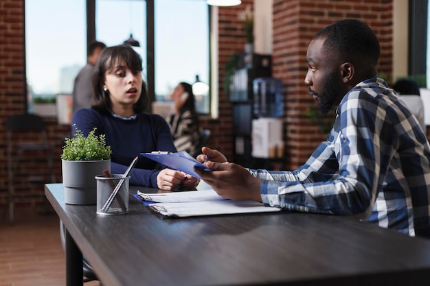 African american recruiter reviewing young adult candidate CV while talking about career opportunity. Business company employer asking woman questions about her work experience in domain.