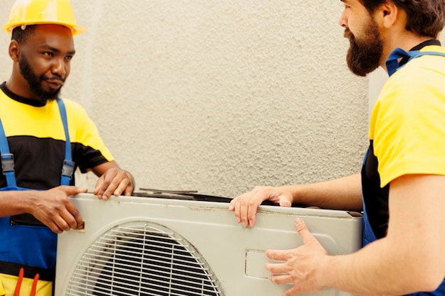 African american repairman and apprentice worker pulling apart old defective outdoor hvac system to replace it with new performant condenser after draining refrigerant and replacing ductwork