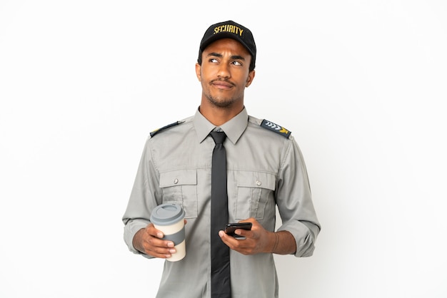 African American safeguard over isolated white background holding coffee to take away and a mobile while thinking something