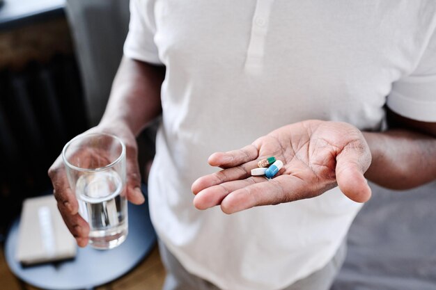 African american senior man with glass of water and three pills on hand