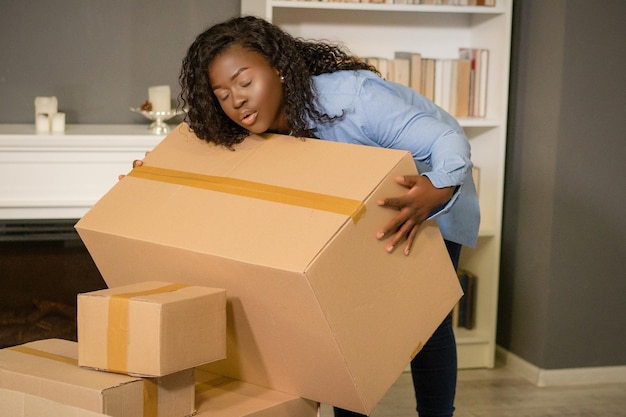 African american woman in a blue shirt carries cardboard boxes in her new home she has a relocation ...