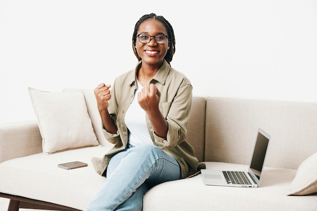 African American woman business freelancer working sitting on sofa at home in laptop and phone business calls and correspondence happiness smile home clothes eyeglasses light interior background