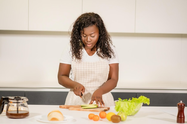 African american woman makes a vegetables salad for a snack wavy hair girl makes breakfast for all f...