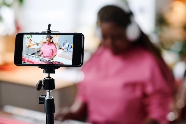 African american woman recording her performance on piano on smartphone sitting in the room