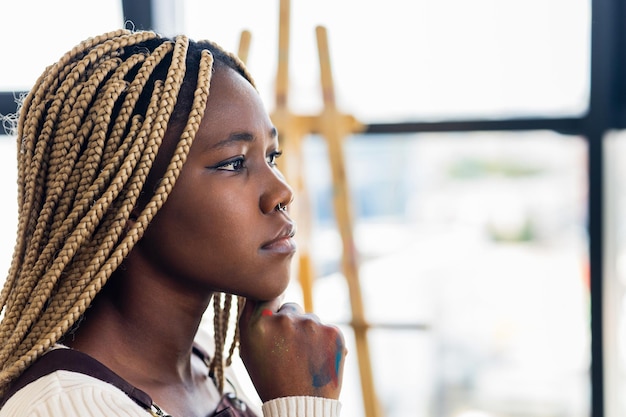 African american woman sitting next to blank white canvas on easel in workspace