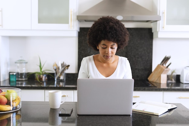 African american woman sitting in kitchen using laptop