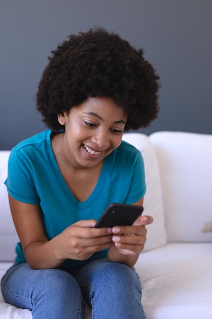 African american woman sitting on sofa using smartphone