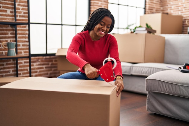 African american woman smiling confident packing cardboard box at new home