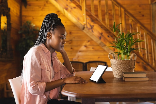 African american woman spending time in log cabin and having tablet video call with copy space. Log cabin, nature and lifestyle concept.