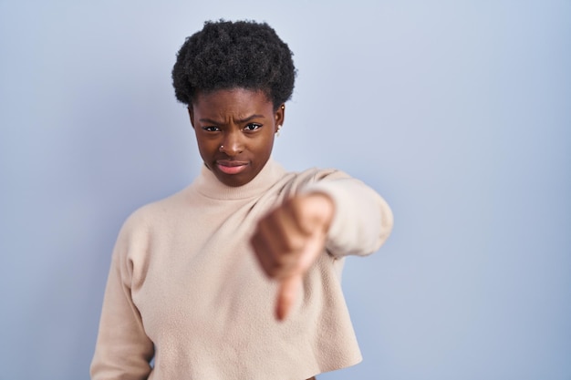 African american woman standing over blue background looking unhappy and angry showing rejection and negative with thumbs down gesture. bad expression.