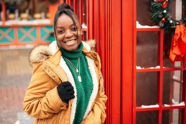 African american woman standing street outside near Christmas Tree fair market, red telephone box