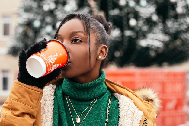 African american woman standing street outside near Christmas Tree hold cardboard cup