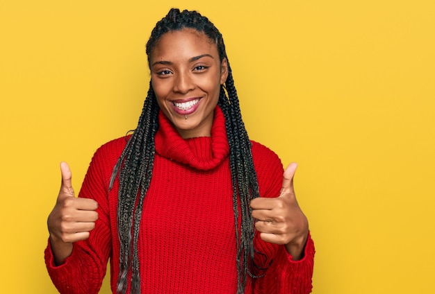 African american woman wearing casual winter sweater success sign doing positive gesture with hand thumbs up smiling and happy cheerful expression and winner gesture